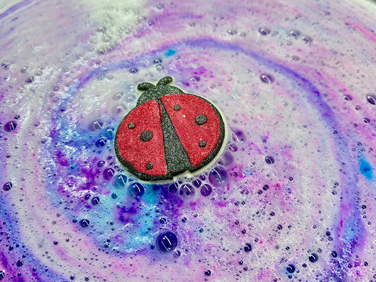 Make bath time bloom with our handmade Lady Bug Bath Bomb! Bursting with hidden colors and fragranced in a vibrant blend of wild berries, mandarin, jasmine, honeysuckle, vanilla praline, and soft amber woods. A sweet and playful bath treat inspired by garden florals and summer magic. Phthalate-free and fun for all ages!